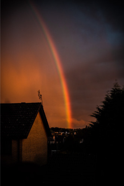 A rainbow in a moody sky with a house and tree in the foreground