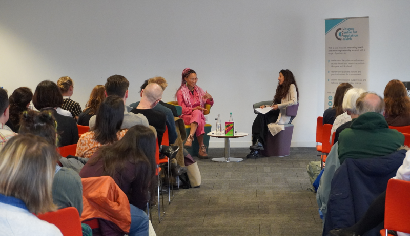 Mikaela Loach and Zarina Ahmad in conversation, sitting around a small round table, in front of an audience.