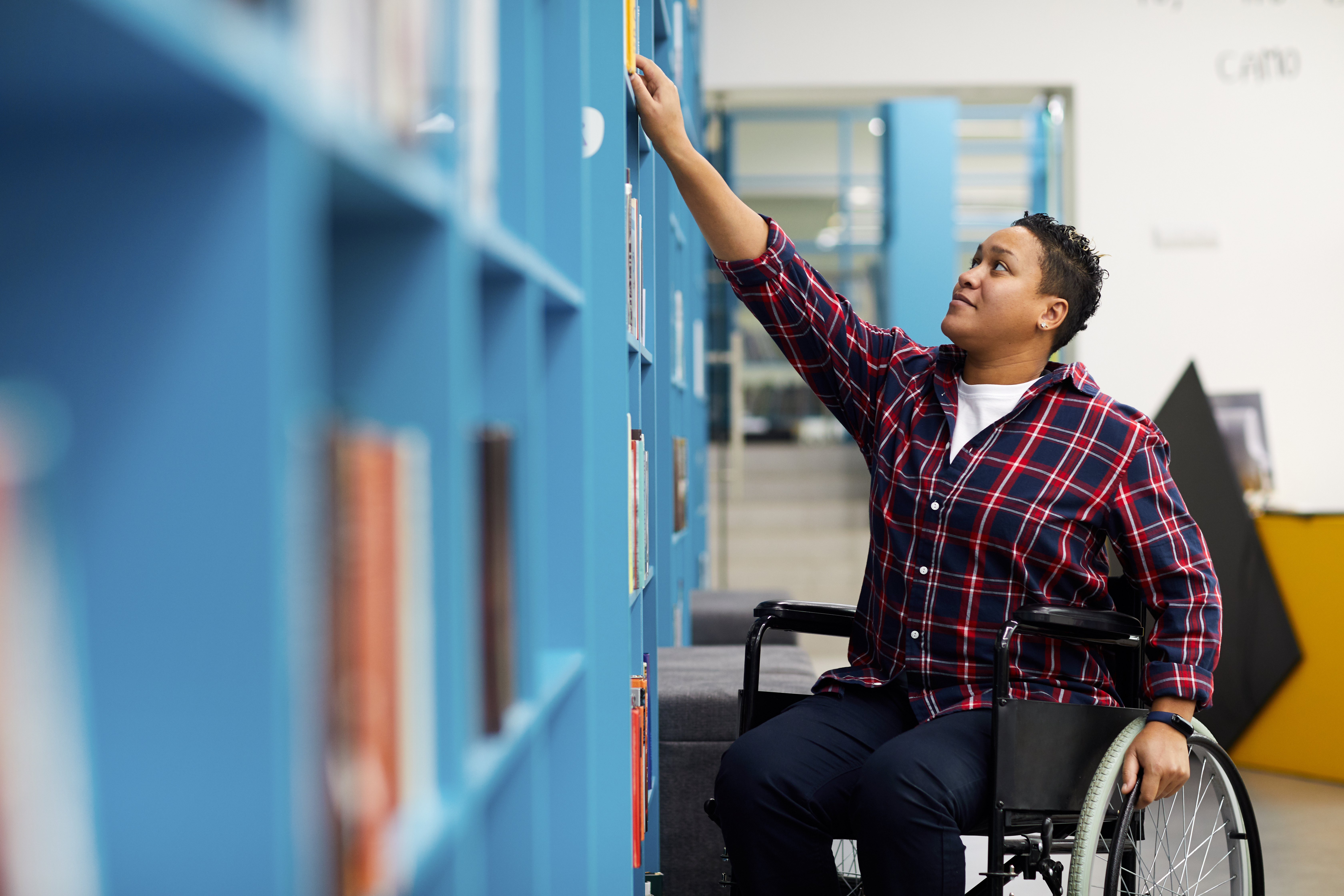 Person in a wheelchair in the library, reaching for a book.